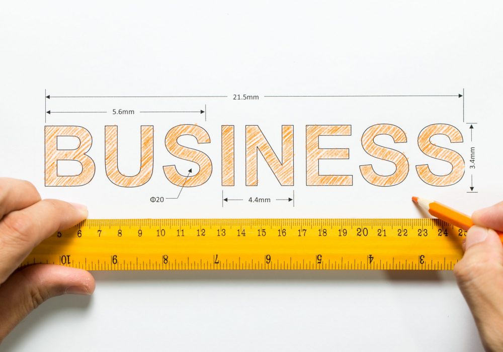 Hand holding ruler and pencil measuring the word business